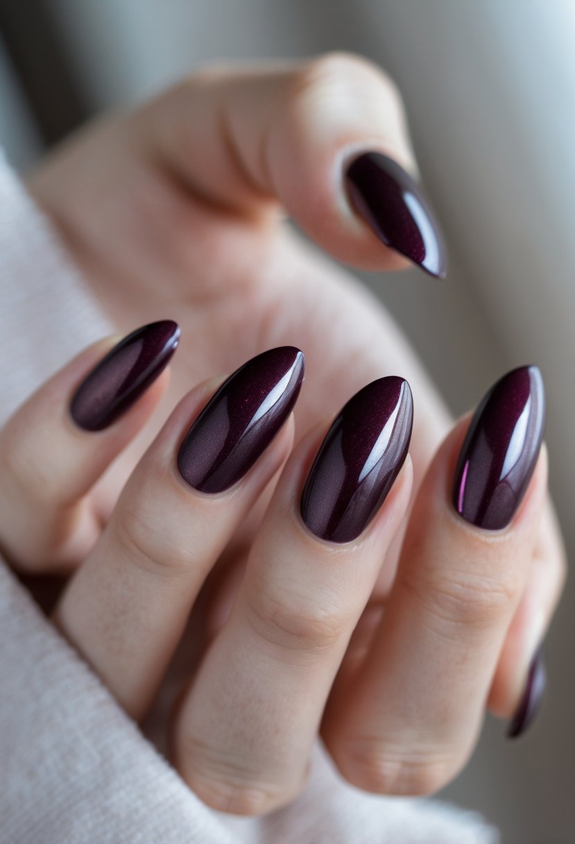 Close-up of a hand with dark wine-colored chrome gradient nails against a neutral background.