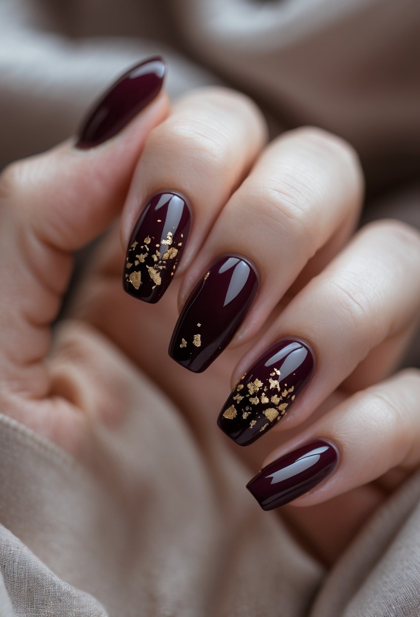 A close-up of a hand with burgundy nails decorated with gold flakes resting on a neutral background.