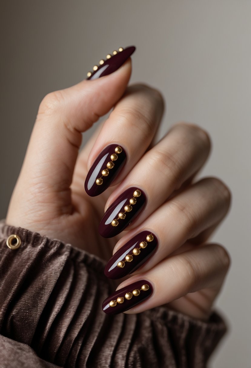 Close-up of a hand with wine red nails decorated with gold studs.