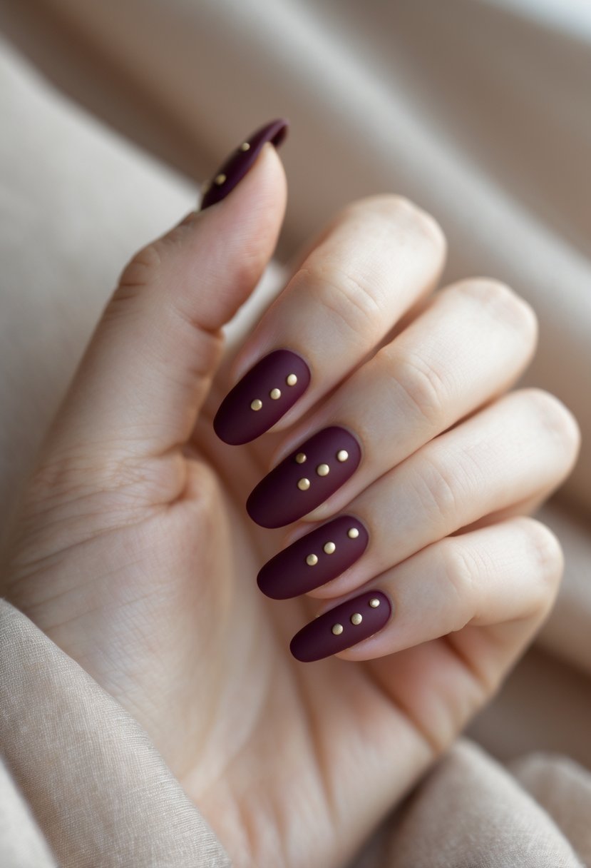 Close-up of a hand with matte burgundy nails decorated with small gold dots.