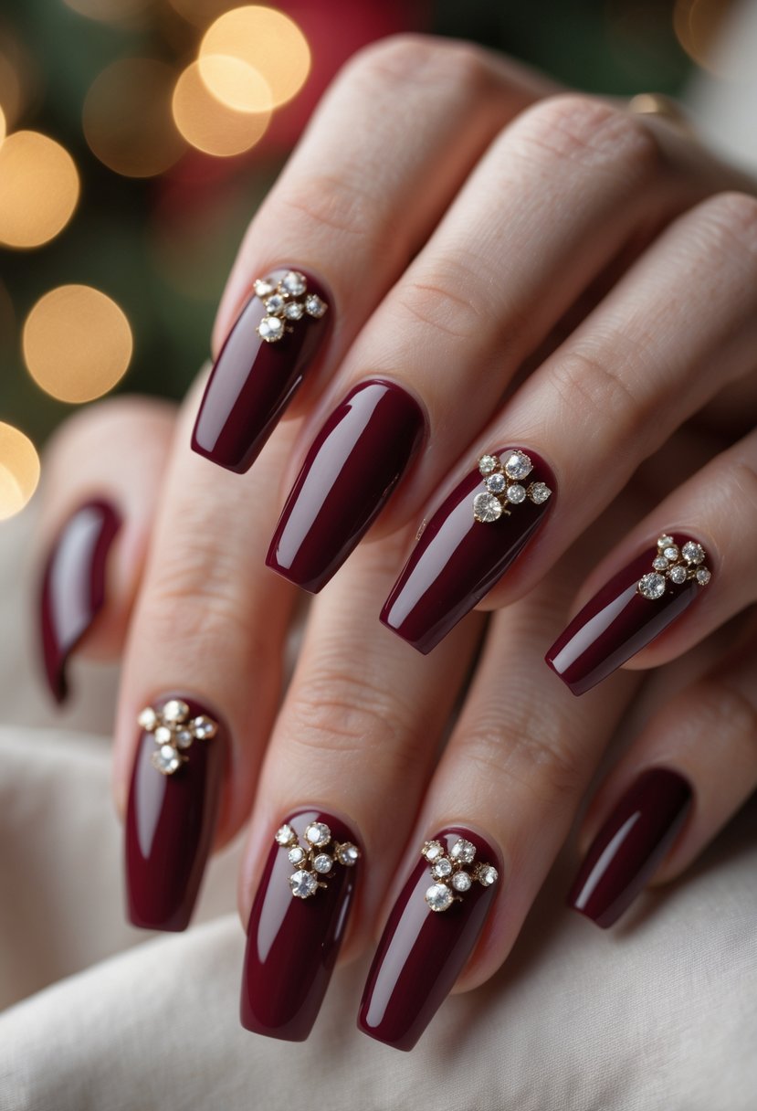 Close-up of a hand with glossy burgundy nails decorated with rhinestones against a softly blurred festive background.