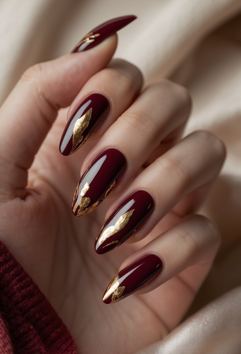 Close-up of hands with red acrylic nails featuring gold foil accents against a soft neutral background.