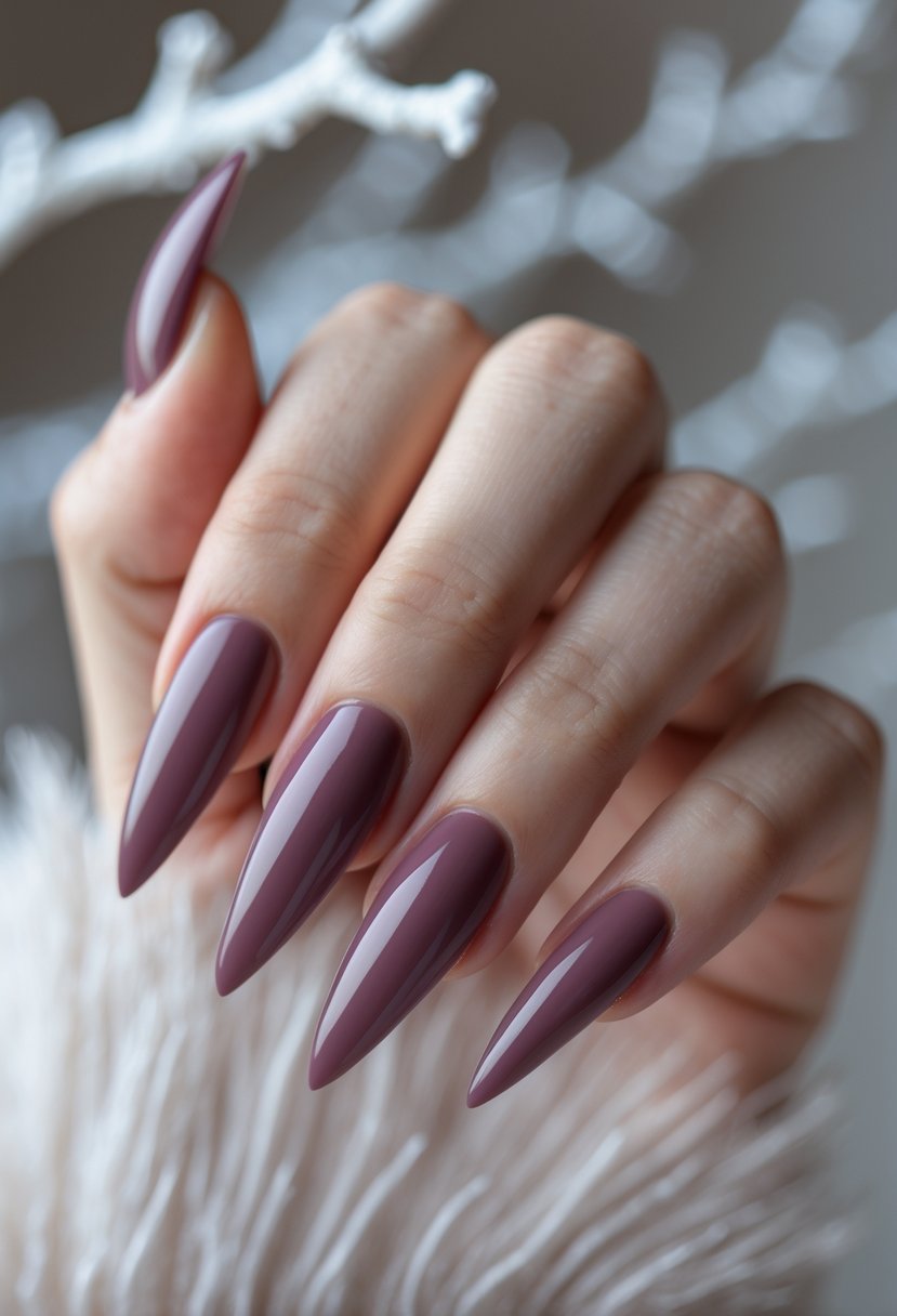 Close-up of hands with deep mauve pink stiletto nails against a soft winter-themed background.
